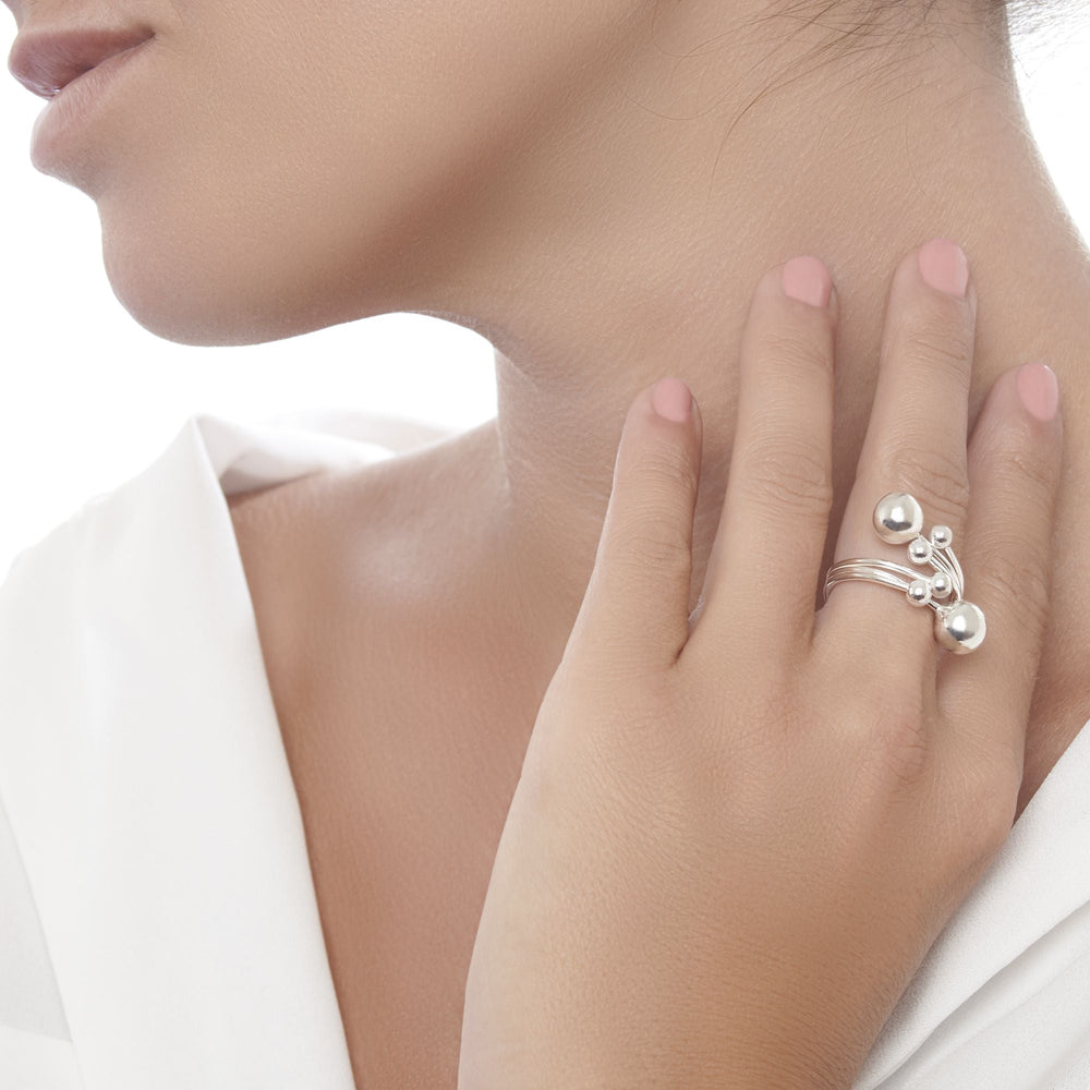A silver ring with multiple spherical embellishments of varying sizes, arranged in an overlapping pattern on female model. 