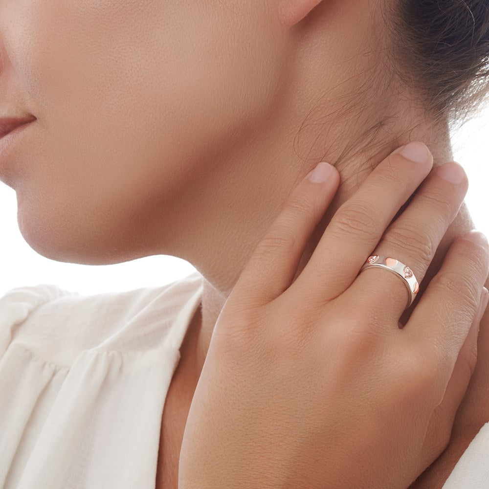 A silver ring with rose gold plated hearts and sparkling cubic zirconia stones set across the finger on female background. 