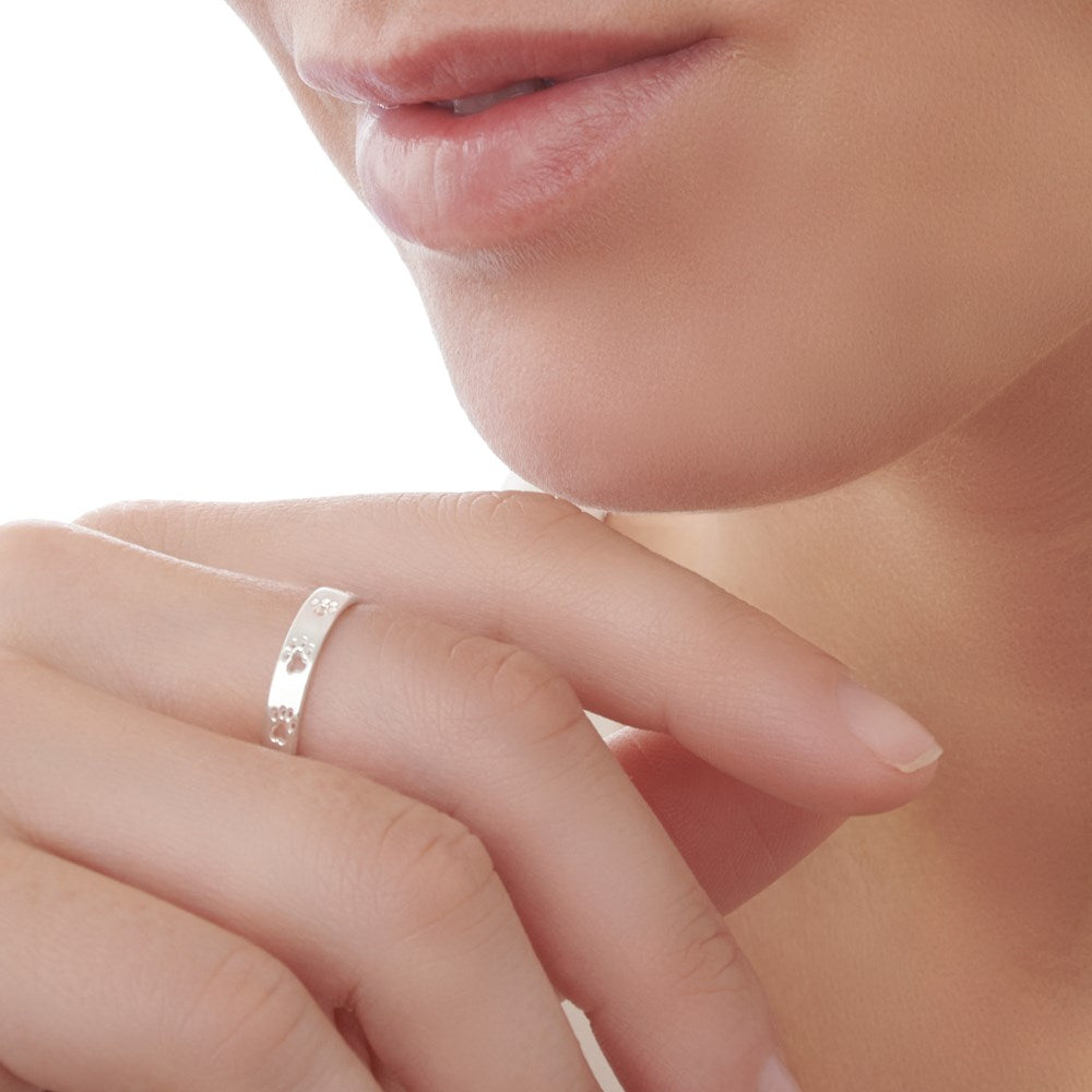 A silver ring with cut-out paw prints walking around the band, displayed against a white background.