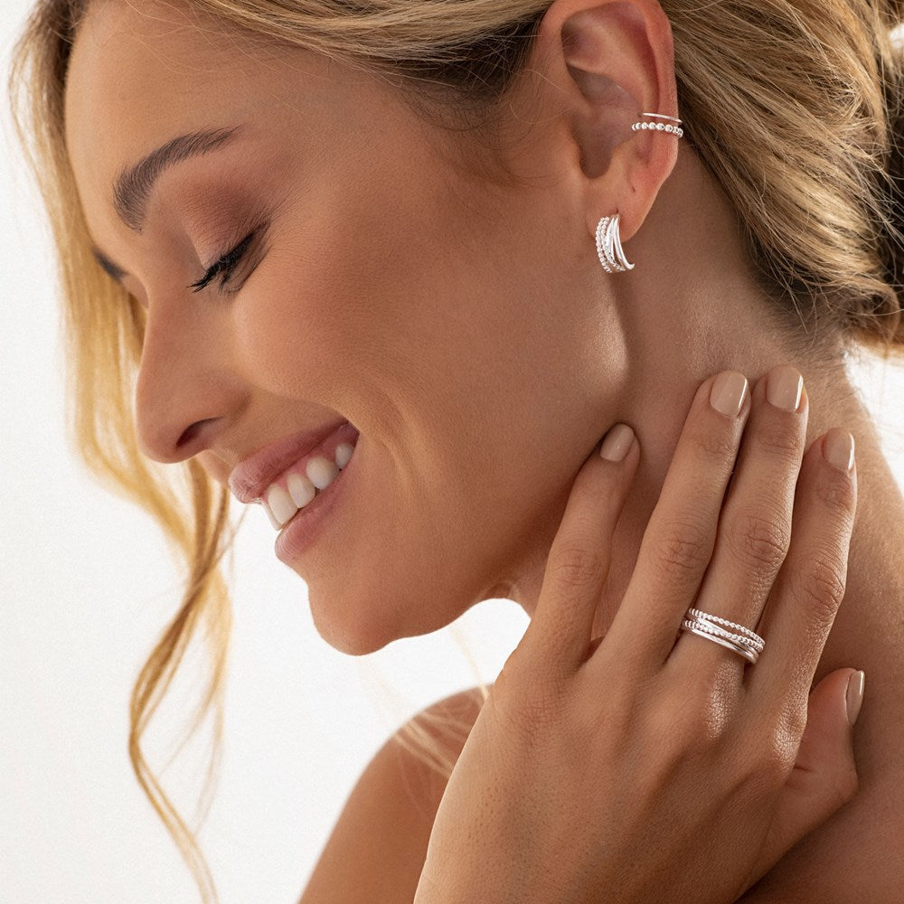 A sterling silver ring with polished and beaded bands, designed to wrap around the finger on female model. 