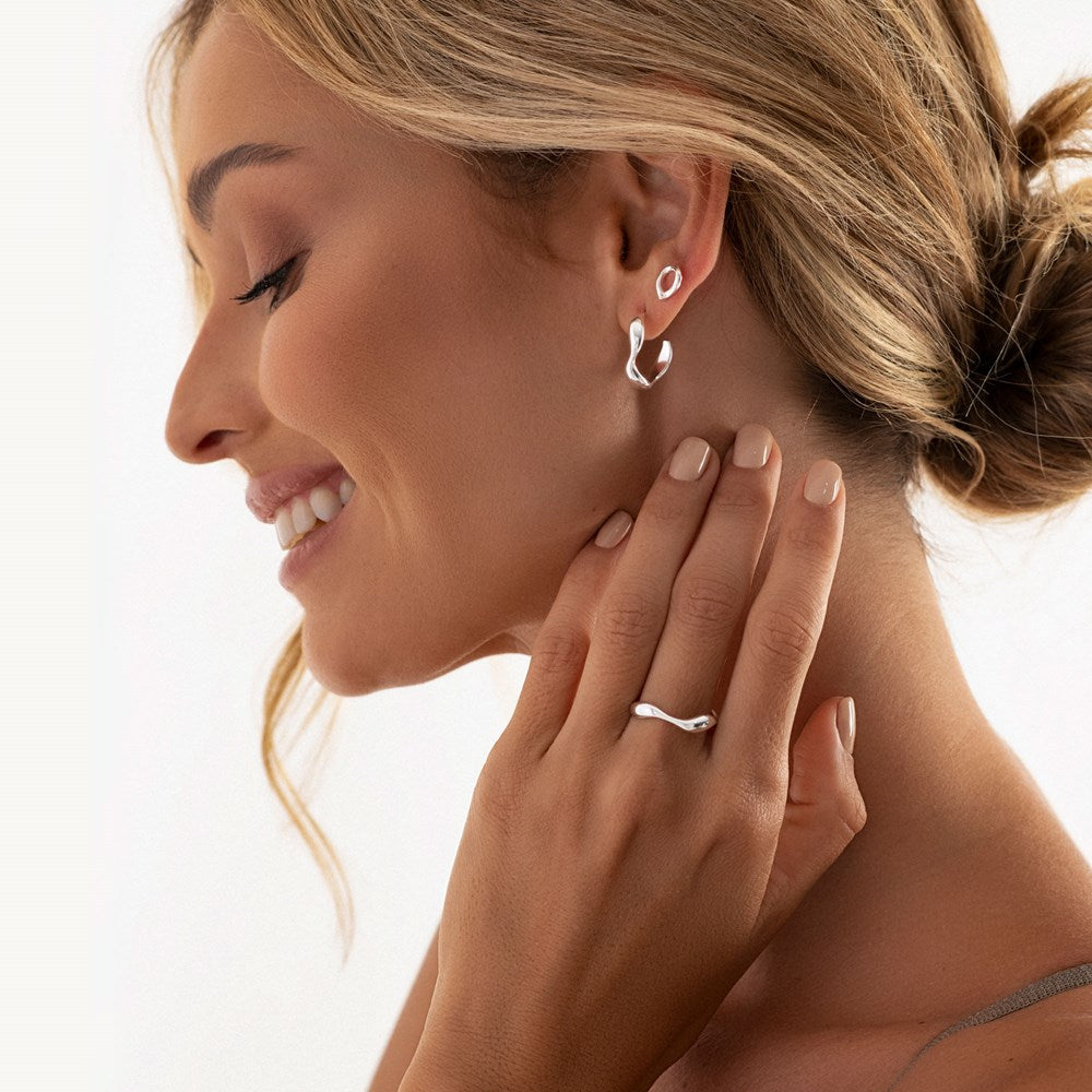 A silver band ring with a fluid, flowing design, giving the appearance of a river on woman model. 