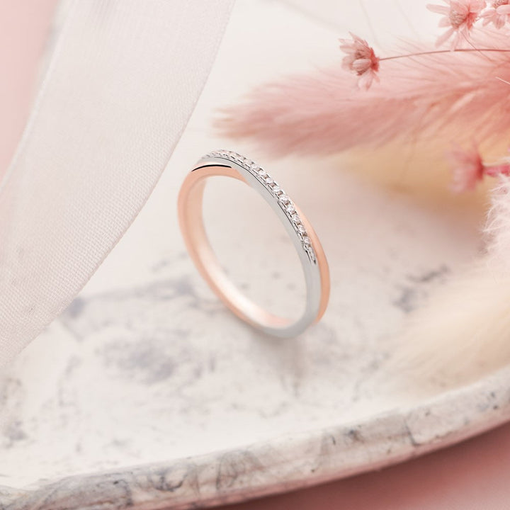 A chic silver and rose gold plated ring with sparkling cubic zirconia stones on the bridge on neutral background. 