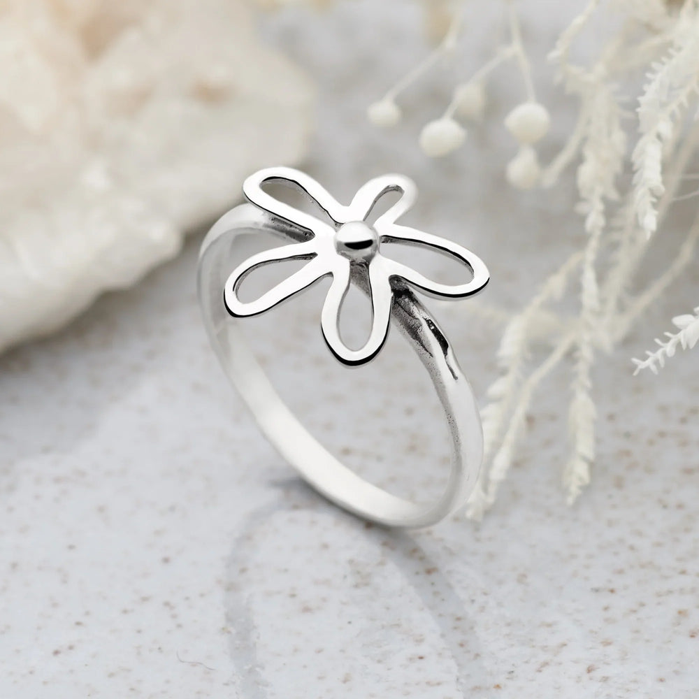 A silver ring with a daisy flower design on the top, featuring a high polish finish on the flower and a satin finish band. Neutral background. 