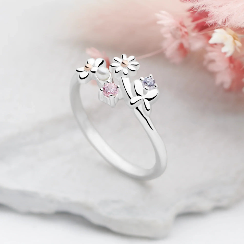 Silver ring with floral designs and gemstones on a soft pink background
