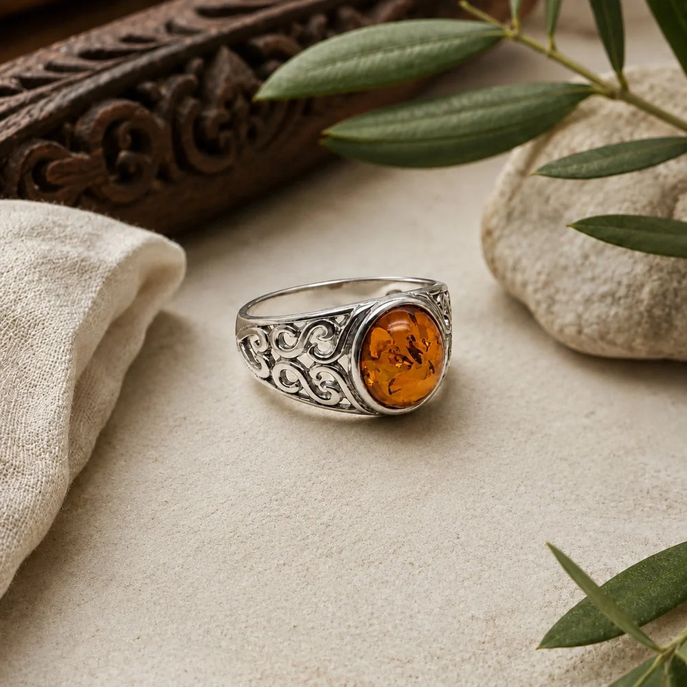 A silver ring with an intricate filigree band and a central oval amber cabochon gemstone.